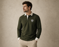 Man wearing a utility green long-sleeve polo shirt with a logo on a beige background